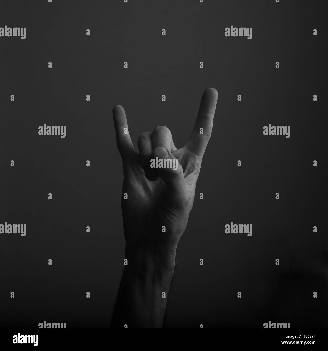 Diavolo maschio avvisatore acustico rock e il gesto a mano contro uno sfondo scuro Foto Stock