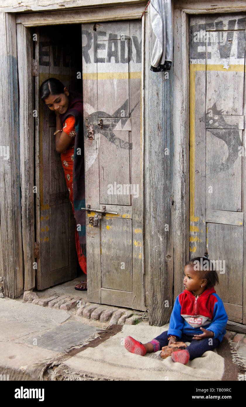 Madre controllo sulla sua giovane bambino seduto su stoop di casa nella città vecchia Dhulikhel, Nepal Foto Stock