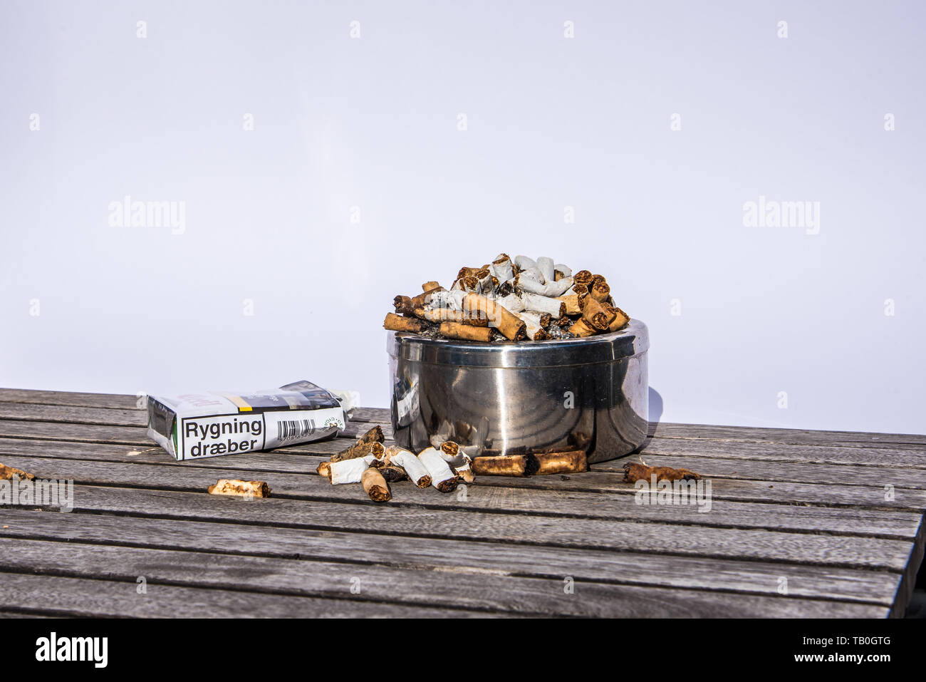 Un posacenere pieno di sigarette e di un pacchetto con il testo il fumo uccide, 29 maggio 2019, Danimarca Foto Stock