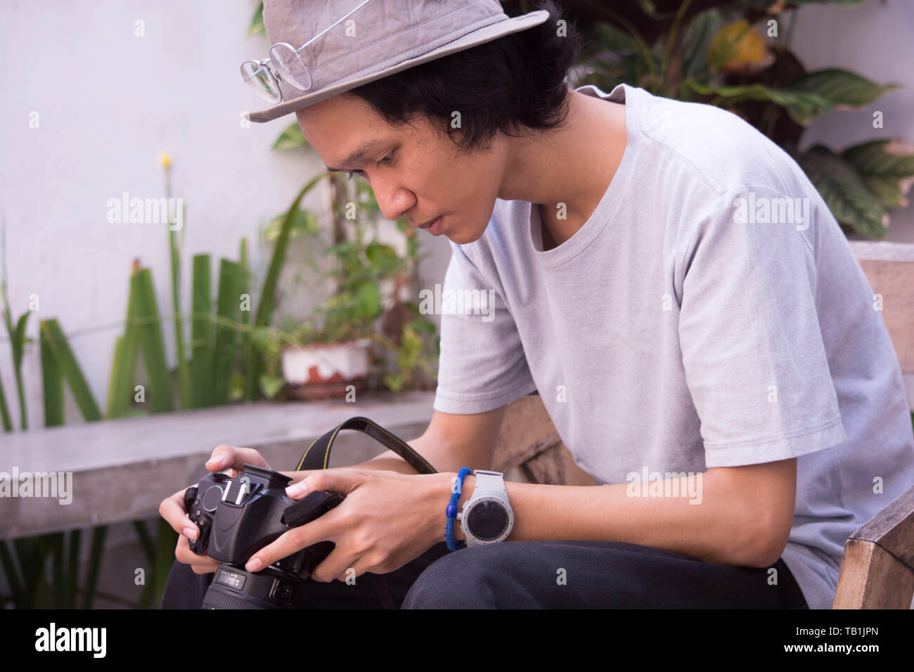 Giovane uomo asiatico con cappello e occhiali holding e rivedere la fotocamera reflex digitale Foto Stock