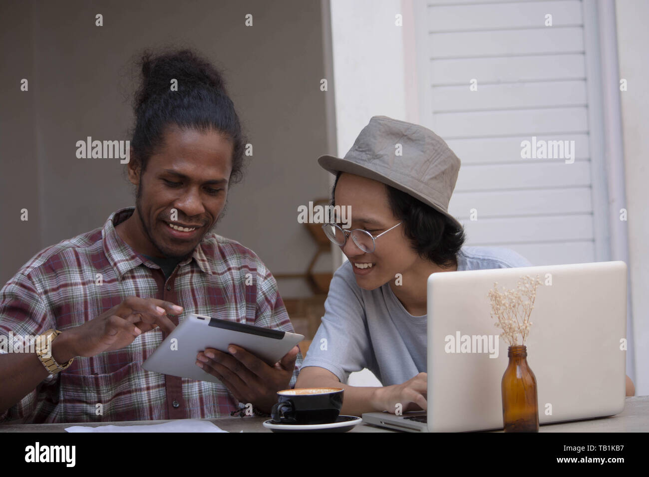 Due giovani uomo creativo discutere con laptop e tablet, giovani asiatici e uomo nero lavora con tablet e laptop in un cafe, Papua e uomo asiatico lavorando Foto Stock