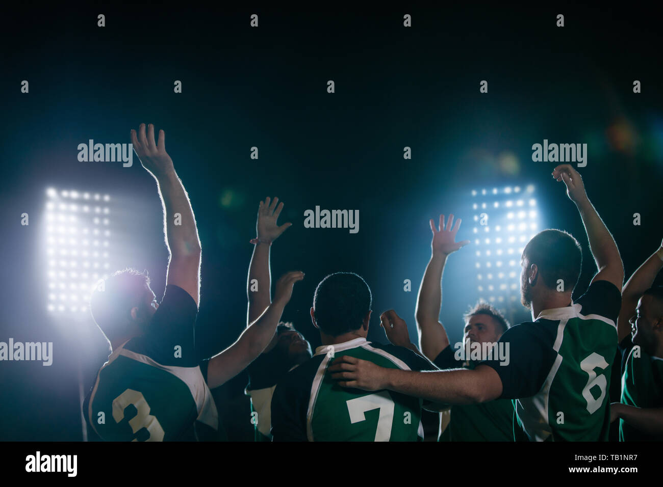 Un gruppo di giocatori di rugby che tifa la vittoria nell'arena sportiva sotto le luci. giocatori di rugby che celebrano la vittoria. Foto Stock
