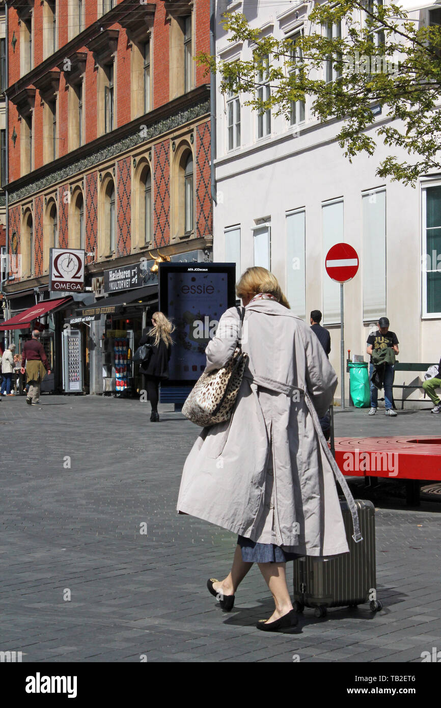 Scena di eleganti donna pedonale che porta una valigia trolley in strada di Copenhagen, Danimarca Foto Stock