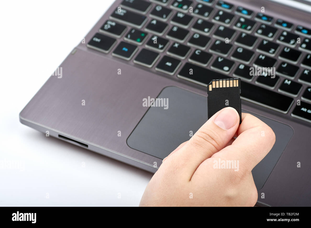 Vista di una donna in possesso di un nero scheda SD nella sua mano. Argento laptop o computer con tastiera nera, isolato su sfondo bianco Foto Stock