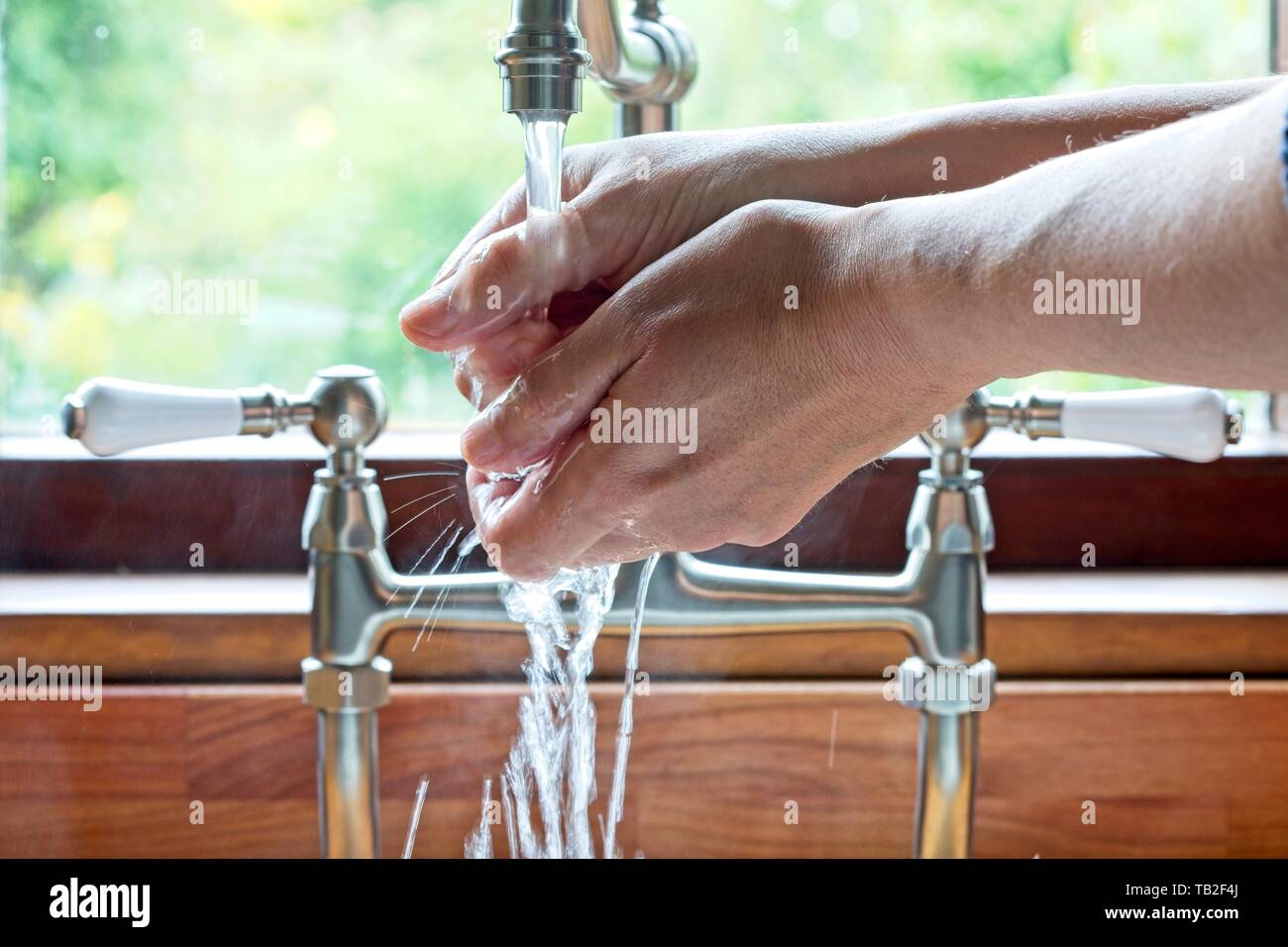 L'uomo lavaggio delle mani sotto i rubinetti ad un lavello da cucina nel Regno Unito. Foto Stock