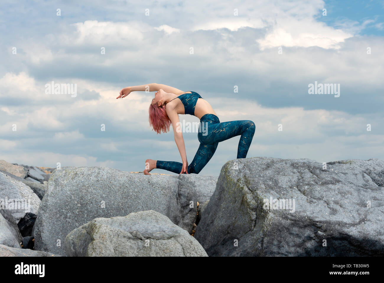 La donna a praticare yoga al di fuori su rocce di granito con drammatico sfondo cielo Foto Stock