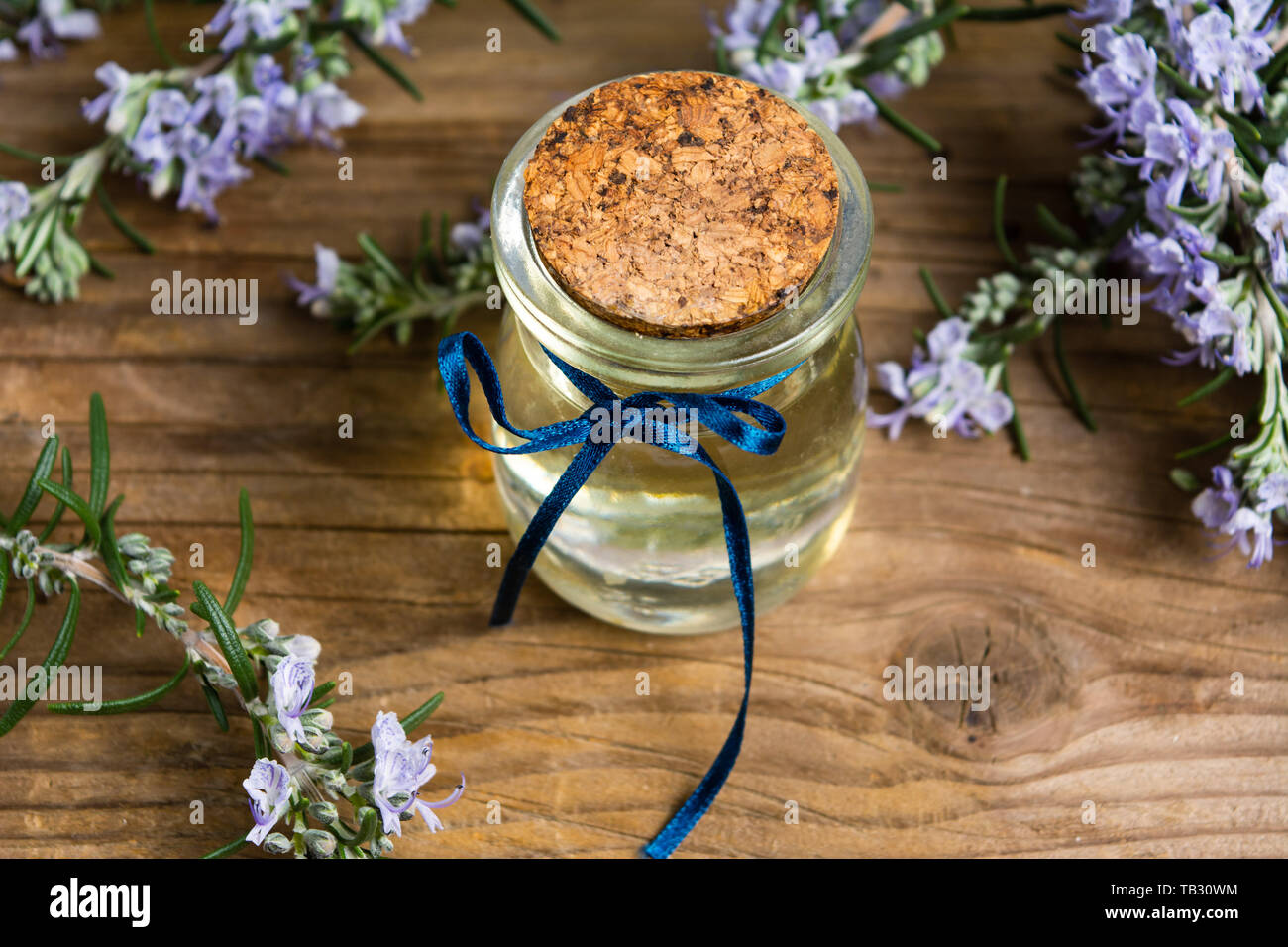Olio di rosmarino in una bottiglia con rami di fiori su un tavolo Foto Stock