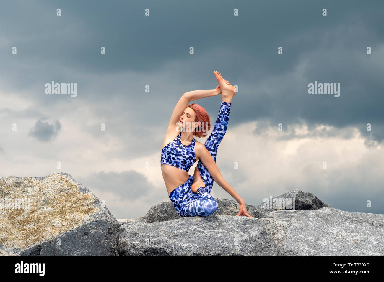 La donna a praticare yoga al di fuori seduta sulle rocce di granito con drammatico sfondo cielo Foto Stock