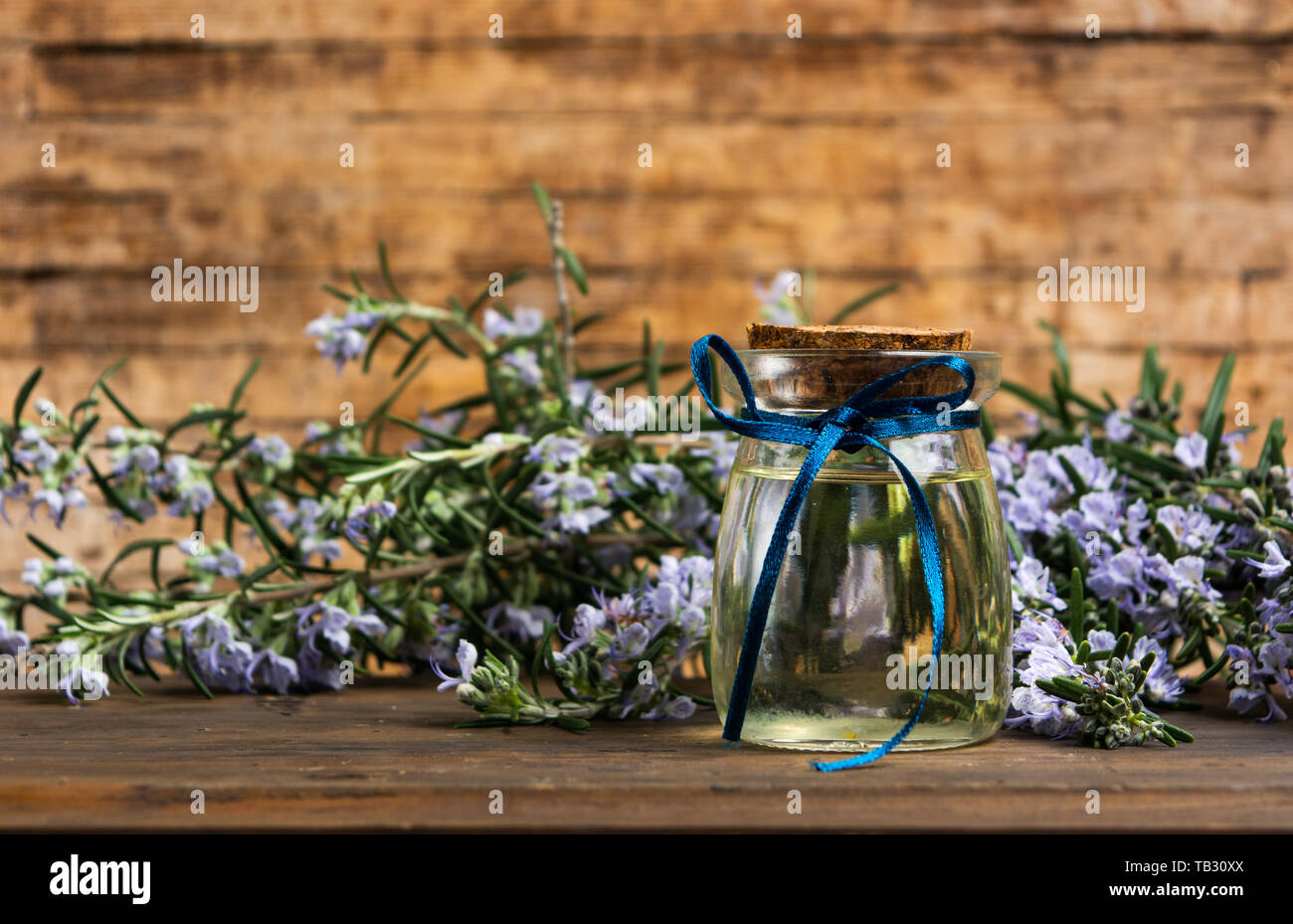 Olio di rosmarino in una bottiglia con rami di fiori su un tavolo Foto Stock