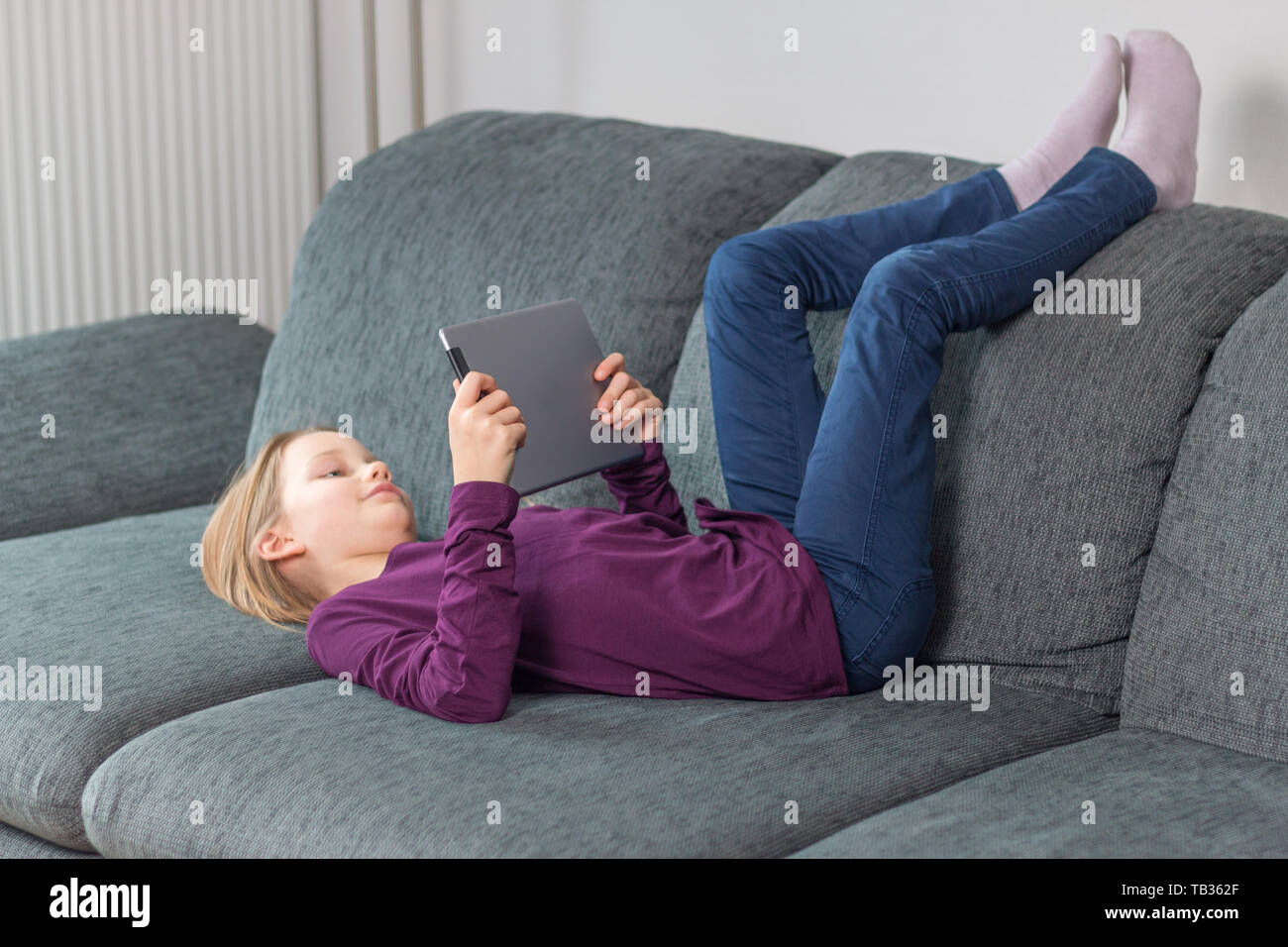 Una ragazza giace sul divano con un tablet PC nelle sue mani Foto Stock