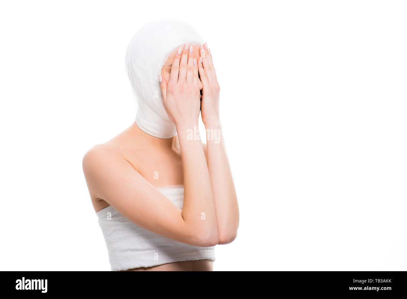 La ragazza con la testa fasciata che ricopre la faccia con le mani isolato su bianco Foto Stock