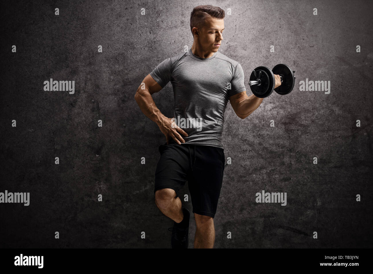 Guy esercizio con un manubrio e appoggiate su un arrugginito muro grigio Foto Stock