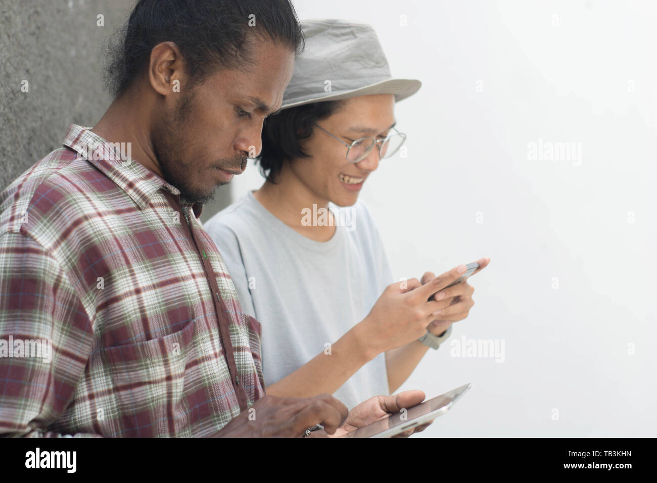 Due uomo utilizza lo smartphone, asiatica e uomo nero migliore amico utilizza lo smartphone e tablet Foto Stock