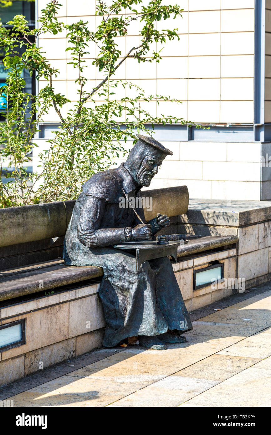 La scultura in bronzo di William Tyndale (2000) lavorando sulla traduzione del Nuovo Testamento in Millennium Square da Lawrence Holofcener, Bristol, Regno Unito Foto Stock