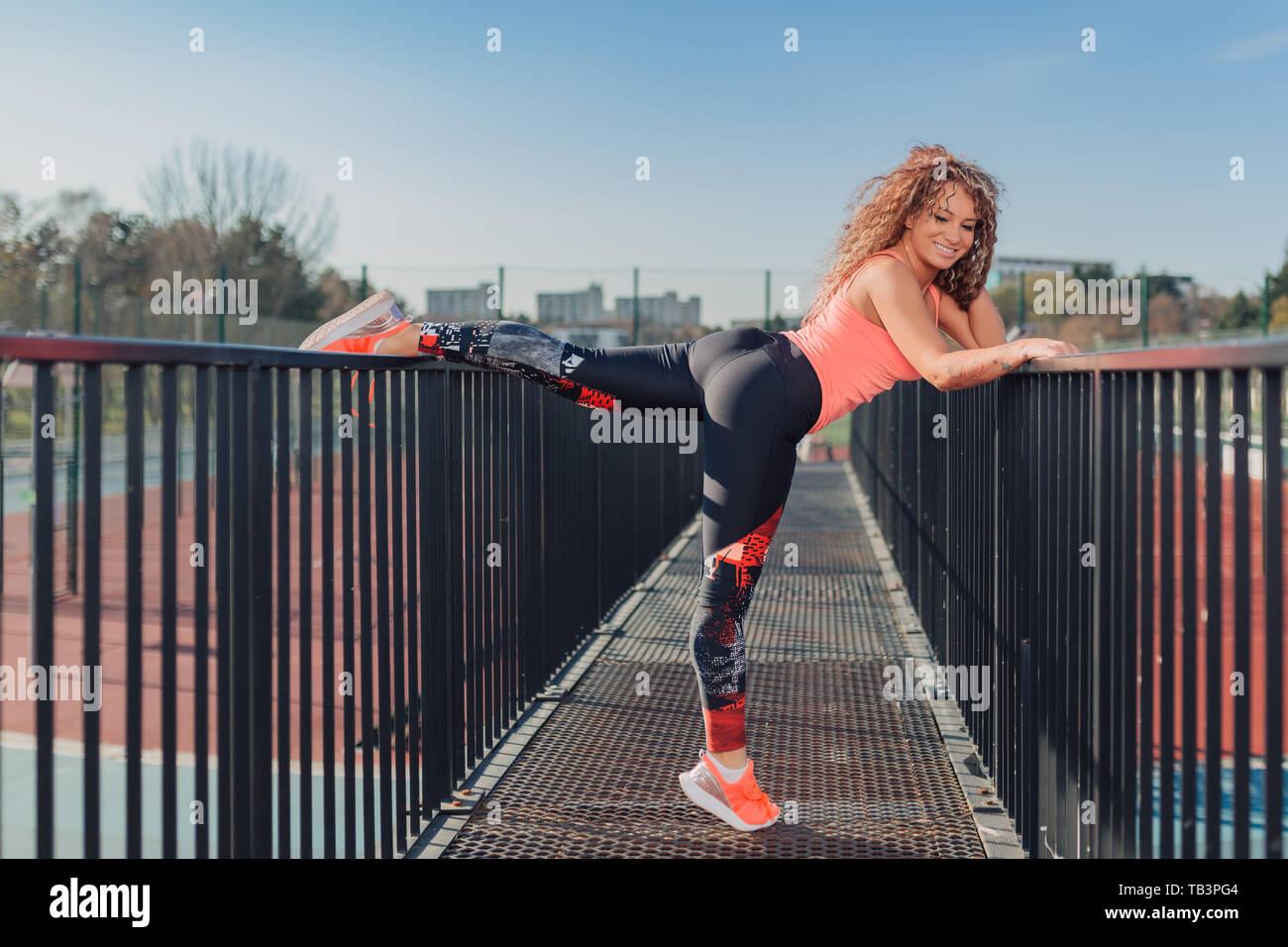 Giovane donna attraente all'aperto godendo di esercizio fisico in ambiente urbano in una giornata di sole mentre si estende su un ponte Foto Stock