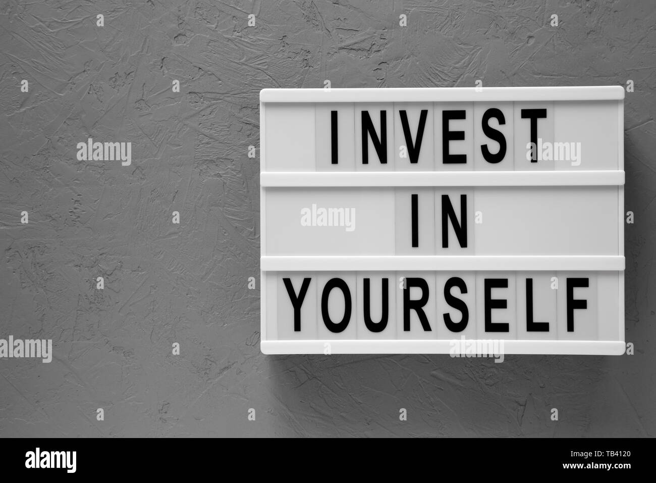 "Investire in te stesso" parole su una scheda moderna su sfondo concreto, vista dall'alto. Il sovraccarico di lavoro piana, laici dal di sopra. Copia dello spazio. Foto Stock