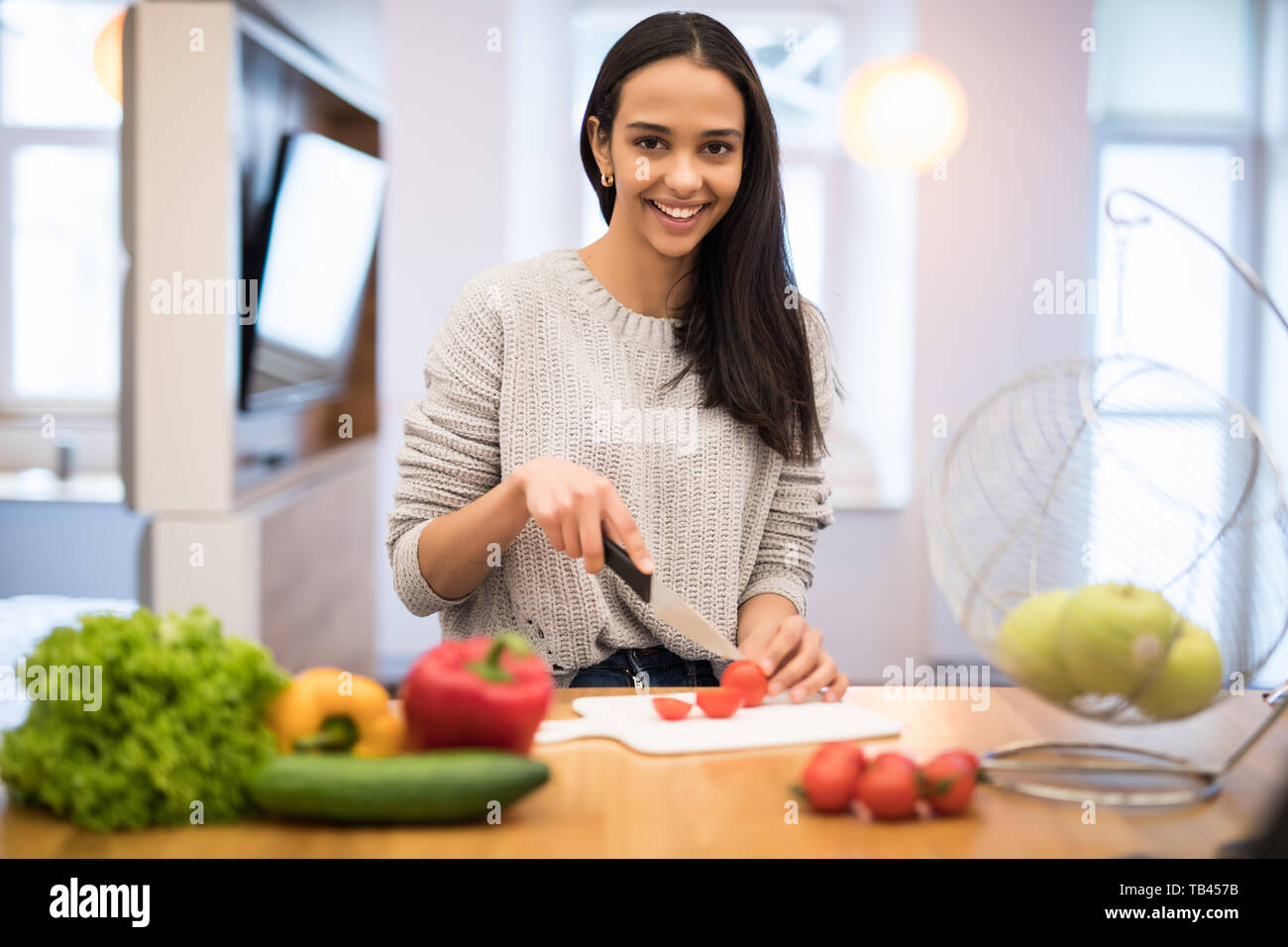 La giovane donna taglia verdure in cucina con un coltello e il computer portatile sul tavolo. Insalata di verdure. La dieta. Concetto di dieta. Uno stile di vita sano. Cookin Foto Stock