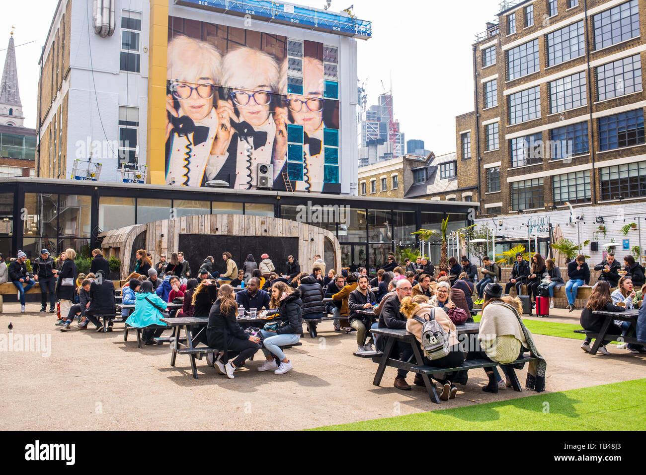 Pop up Outdoor area alimentare con persone mangiare outiside murale e arte di strada celebra Andy Warhol presso la Old Truman Brewery, Ely's Yard, Shoreditch Foto Stock