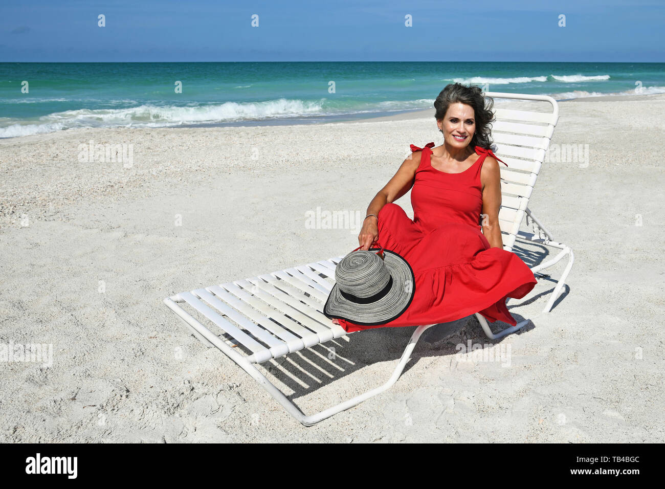 Bella donna in un vestito estivo e Hat seduto sulla spiaggia Foto Stock
