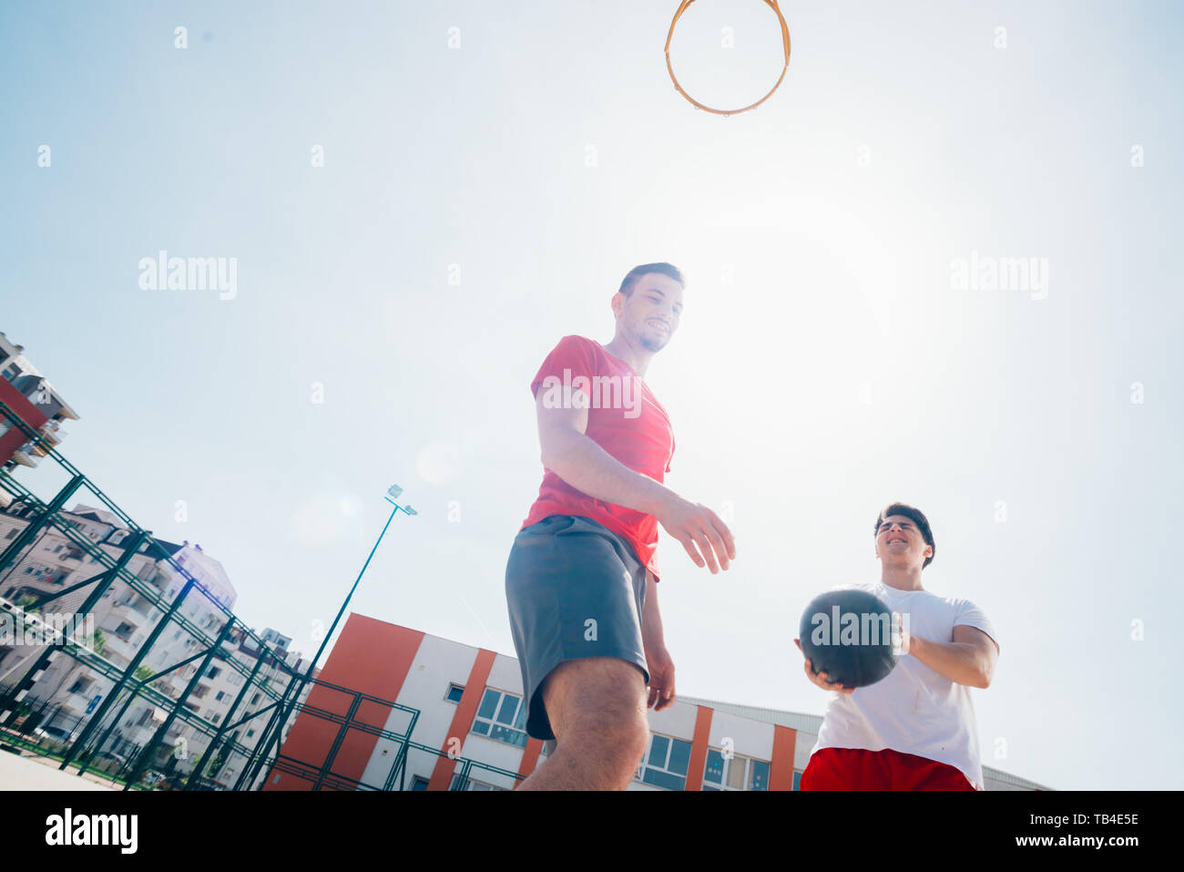 Due amici caucasici indossando rosso dell'apparecchiatura di sport giocando basketballs all'aperto in una giornata di sole mentre essi dribbling e spingere l'altra. Foto Stock
