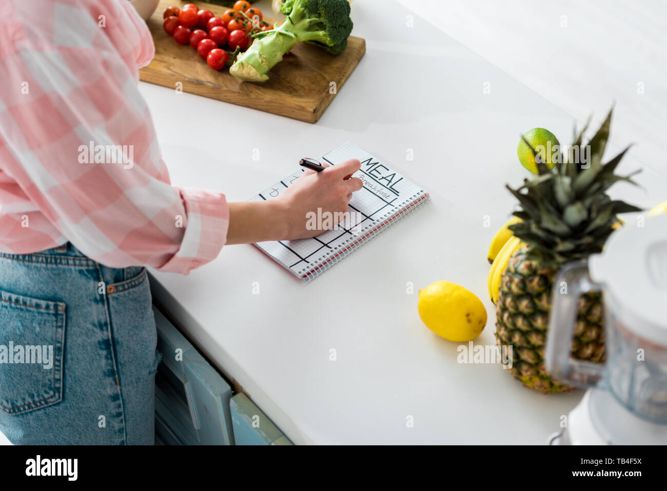 Vista ritagliata della ragazza la scrittura in notebook con pasto scritte nei pressi di gustosi ingredienti in cucina Foto Stock