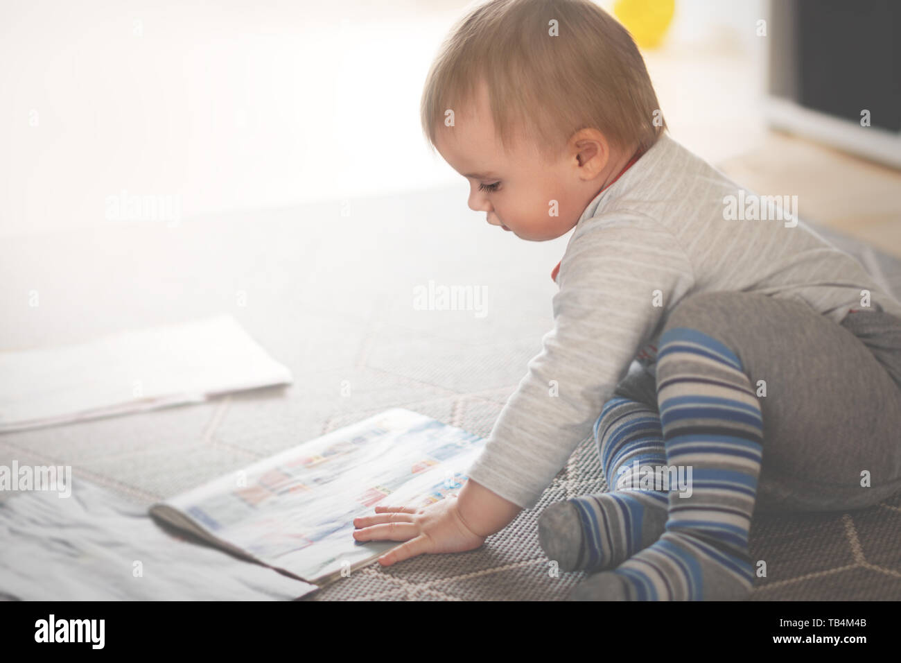 Piccolo Ragazzo è seduto sul pavimento e lettura di riviste, fondale focus Foto Stock