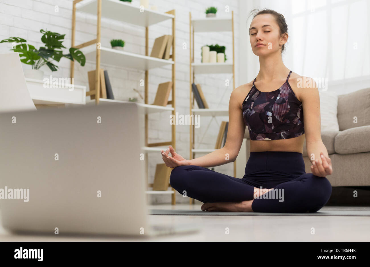 Auto-apprendimento. Donna con notebook per la formazione online di yoga in salotto Foto Stock