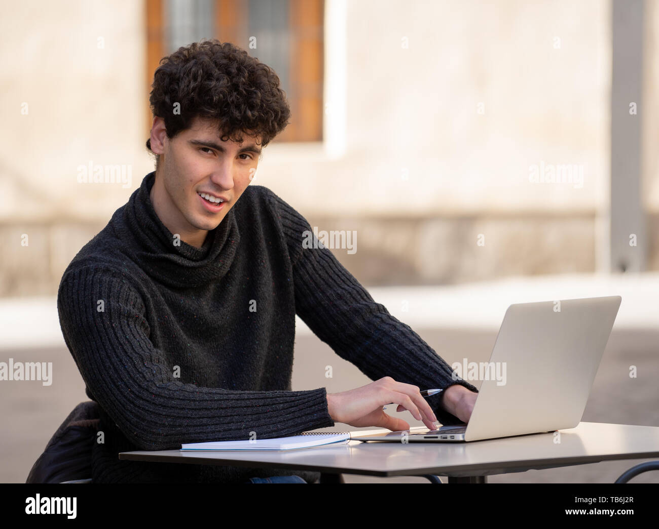 Bel giovane uomo che lavora sul computer portatile terrazza esterna in una città europea coffee shop. Studente sentirsi felice e soddisfatto. In viaggio intorno e Foto Stock