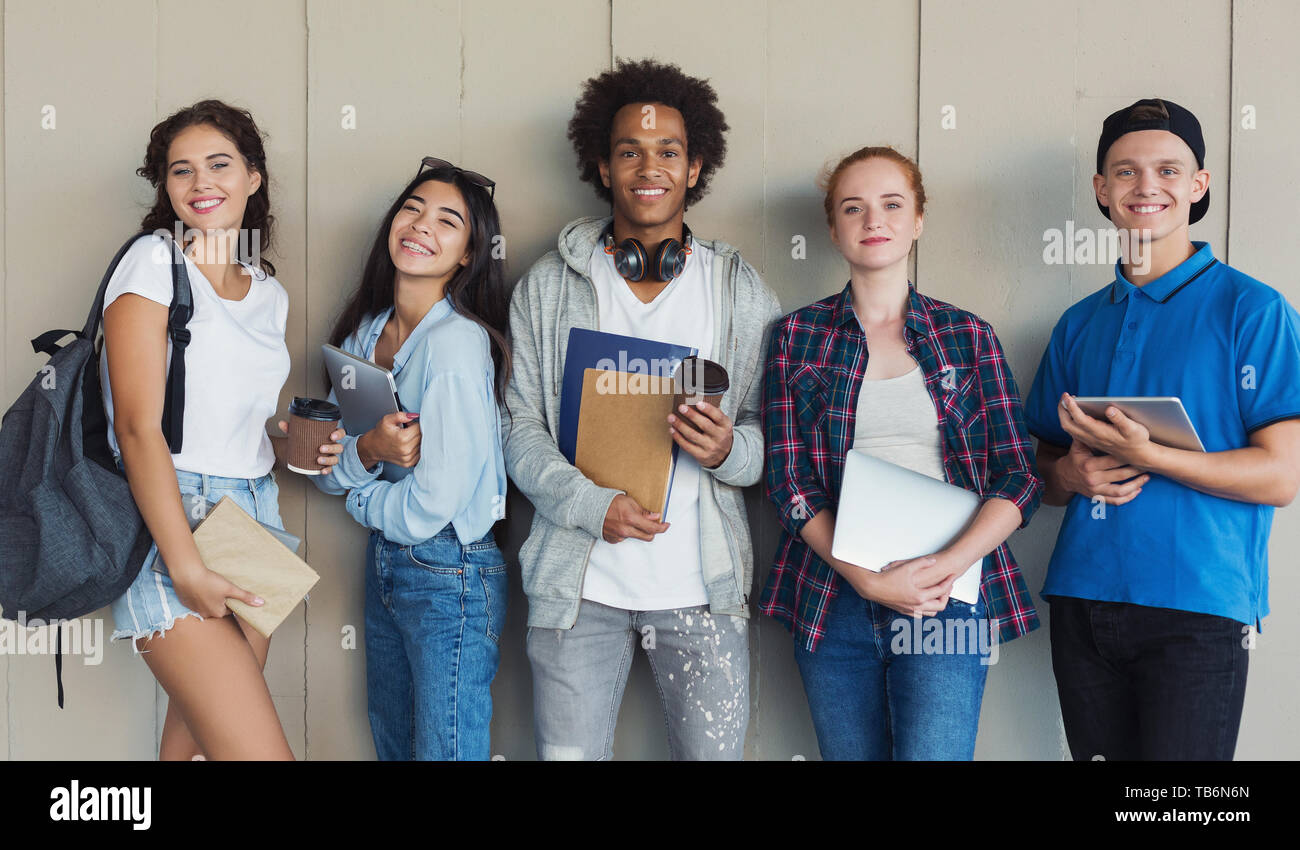 Gruppo etnico studenti adolescenti con cartelle e zaini appoggiata al muro del campus, panorama Foto Stock