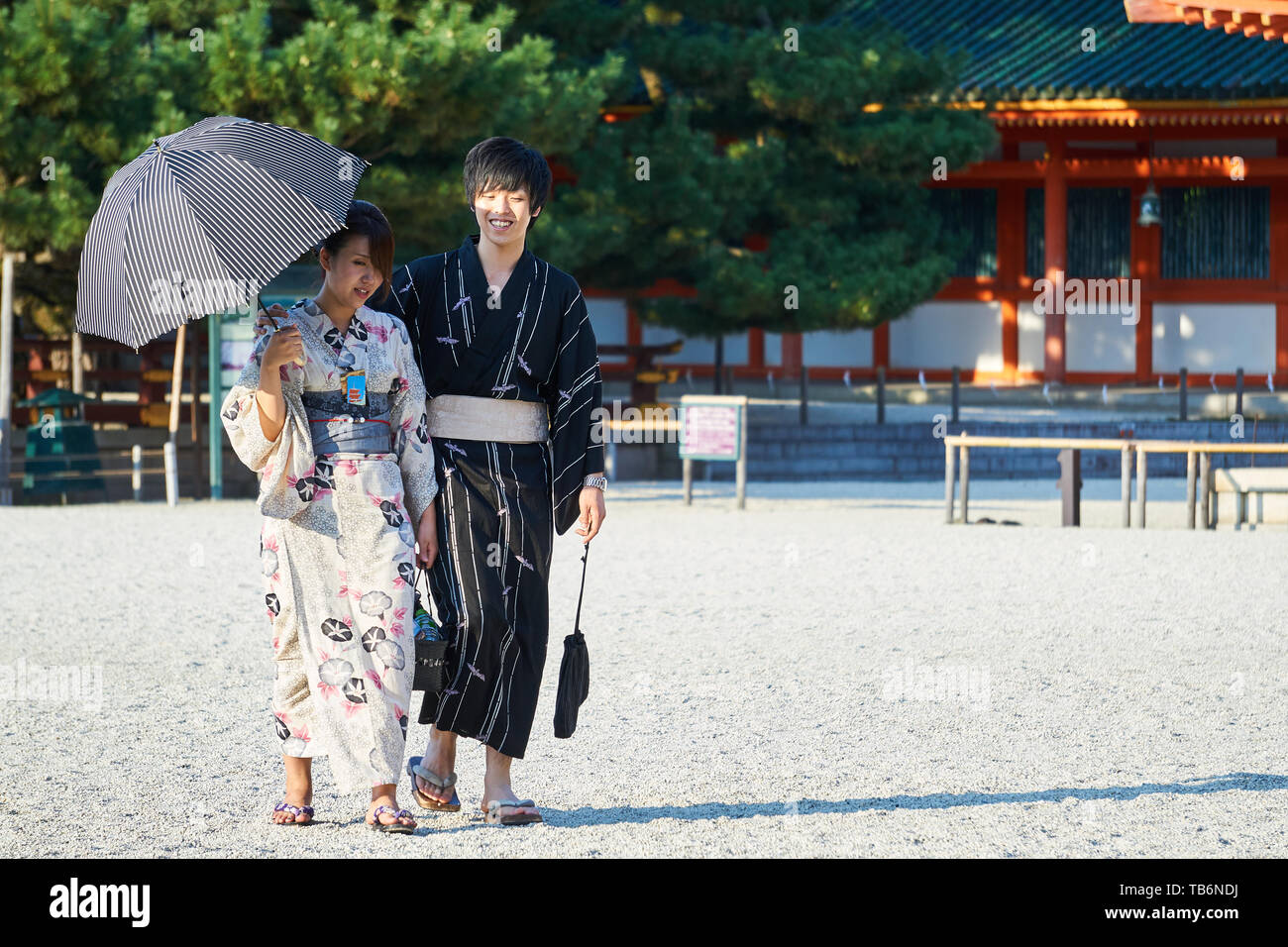 Un turista giapponese giovane vestito in tradizionale kimono yukata cammina insieme sulla sabbia in Heian Jingu's courtyard. La donna tiene un ombrello. Foto Stock