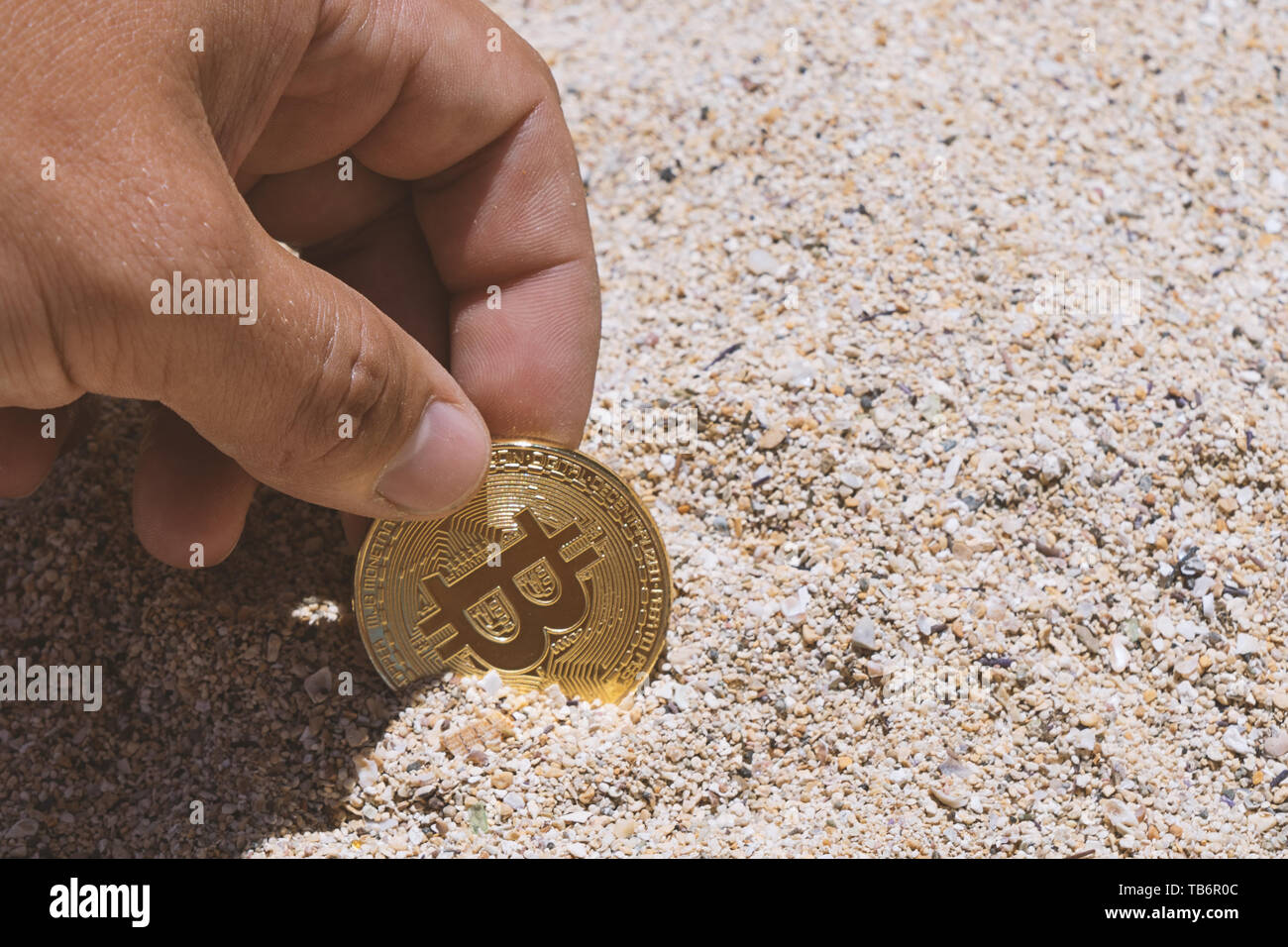 Primo piano di una simbolica bitcoin moneta nella sabbia in man mano. Bitcoin concetto di data mining Foto Stock