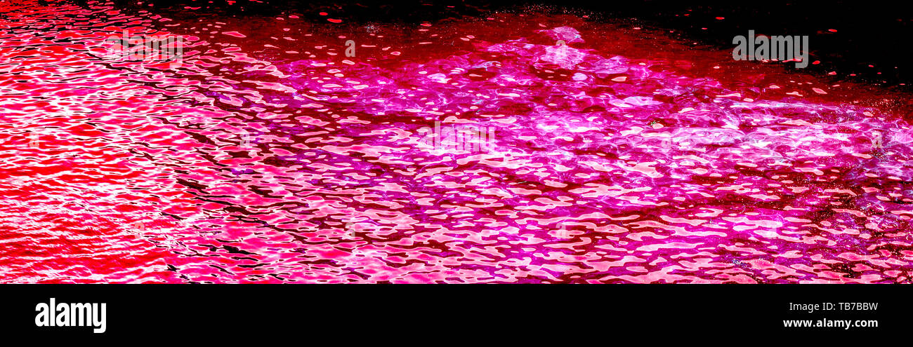 Foto orizzontale di acqua in rosa fucsia, magenta, colore rosso con luce solare riflettente. Foto Stock