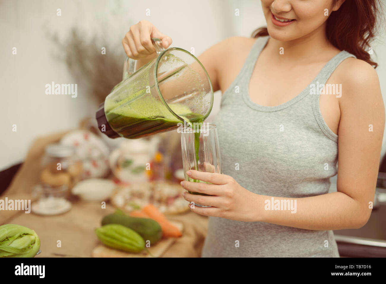 Donna felice versando un cocktail di verde in un bicchiere durante la dieta detox Foto Stock