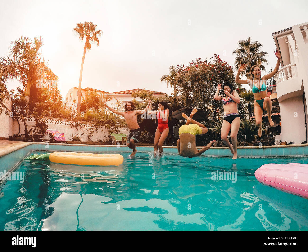 Gruppo di amici felice del salto in piscina al tramonto - Crazy giovani divertirsi facendo parte in esclusiva casa tropicale Foto Stock