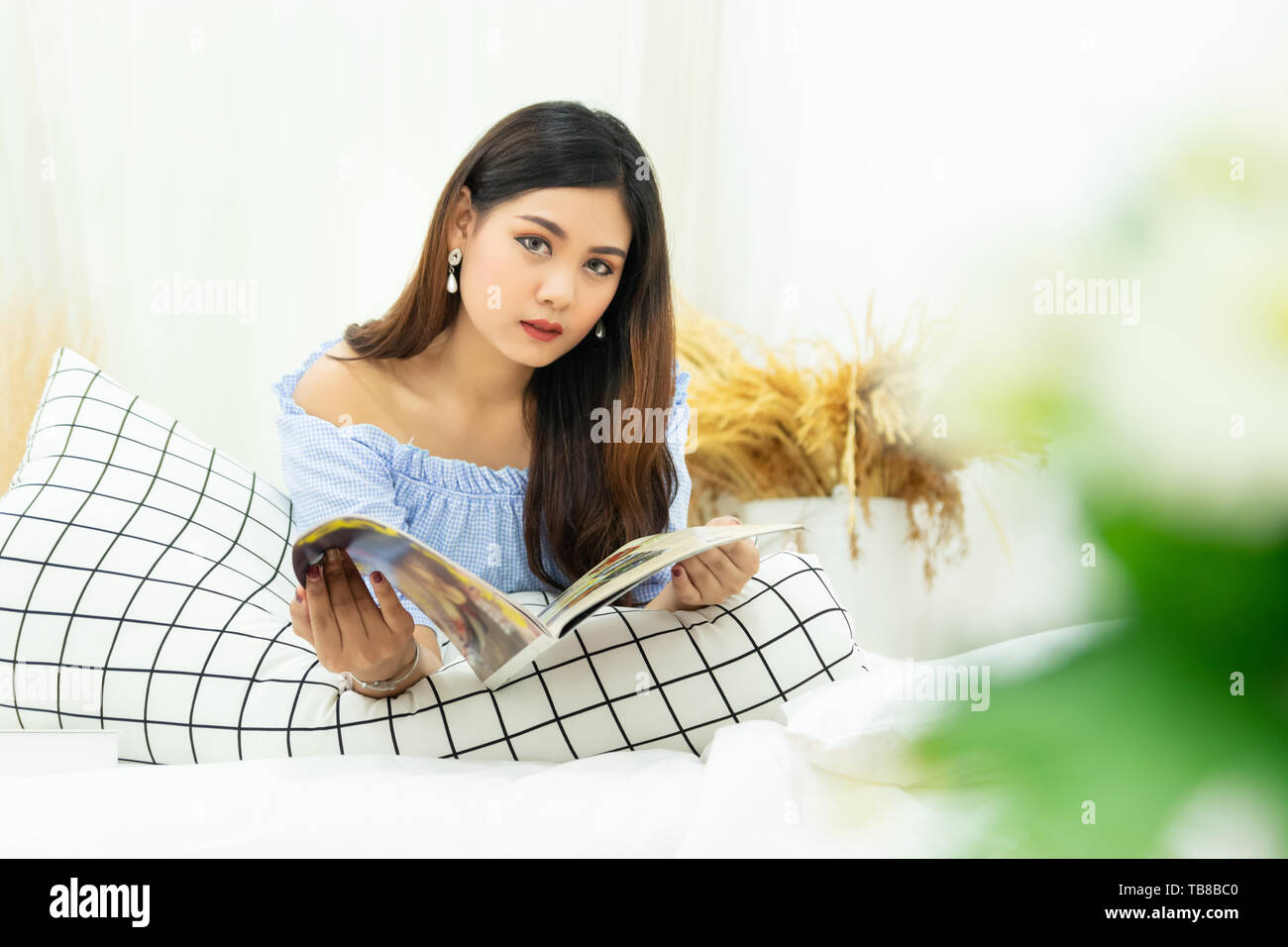 Bella donna asiatica giacente su bianco letto confortevole la lettura di un libro gode del resto al comfort home Foto Stock