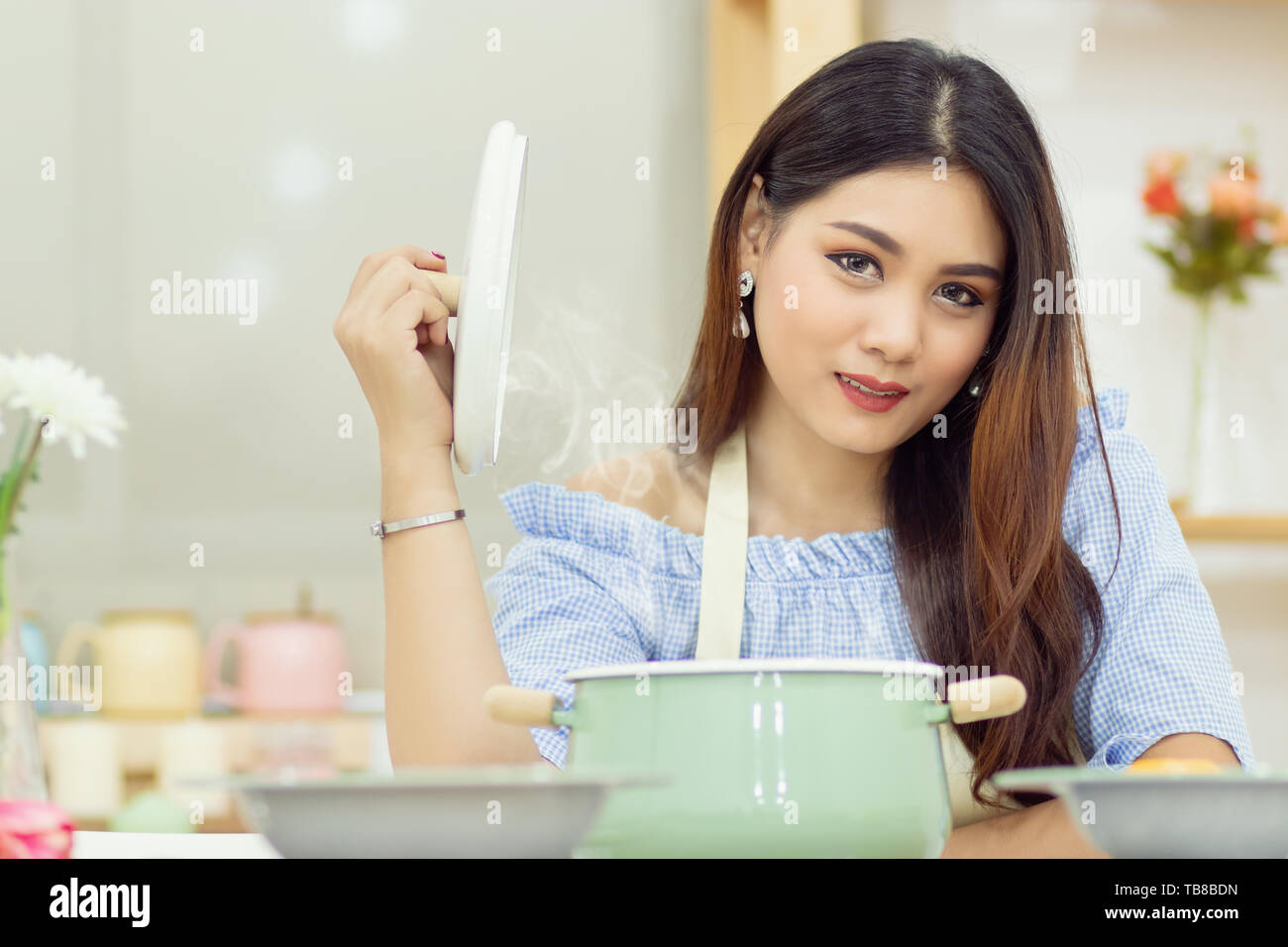 Bella donna asiatica sedersi al tavolo della cucina, aprire il coperchio della pentola di zuppa con il calore del vapore su flottante. Foto Stock