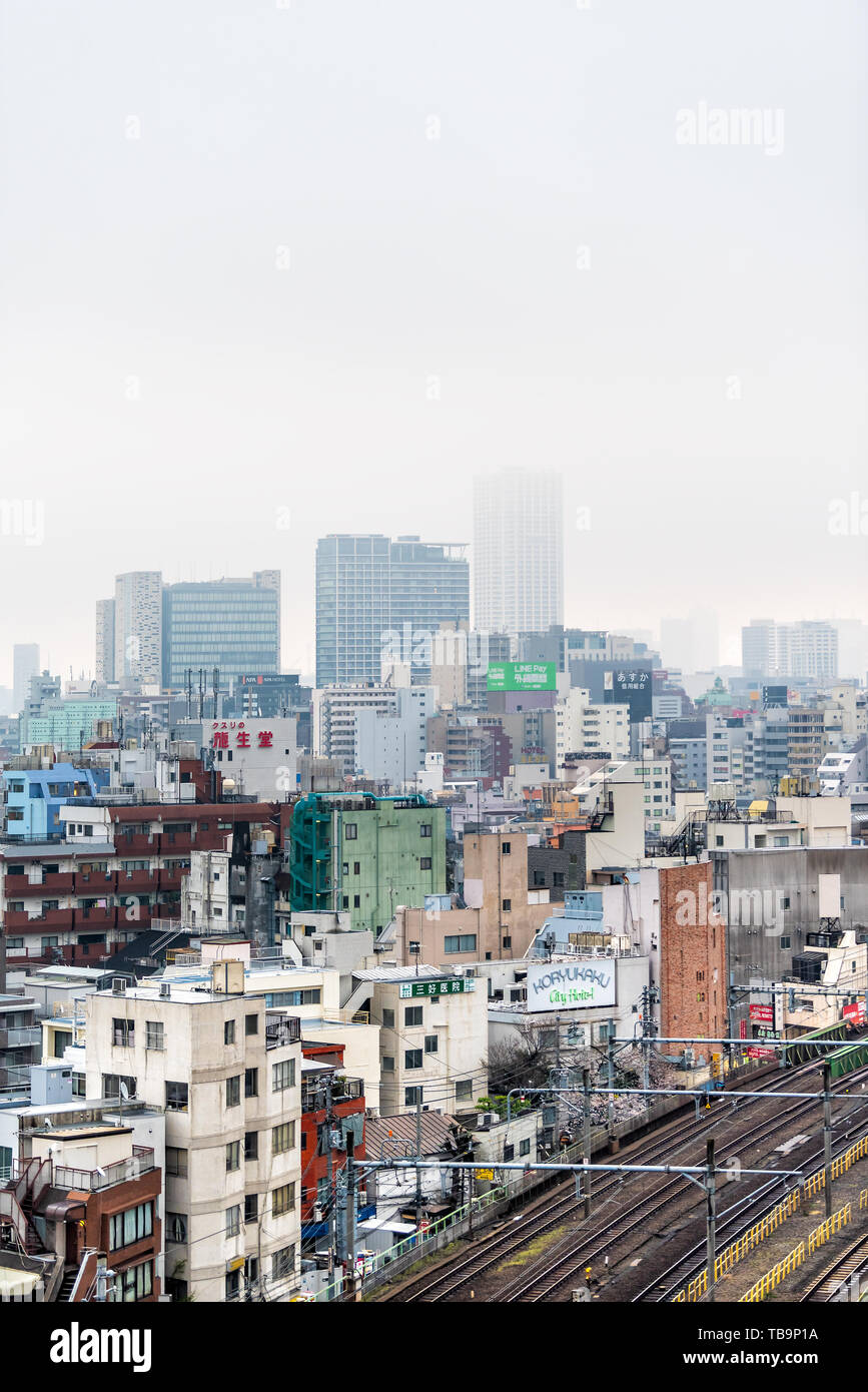 Tokyo, Giappone - 30 Marzo 2019: Shinjuku cityscape vista verticale edifici su nuvoloso nebbia grigio nebbia nuvoloso giorno con molte case e binari del treno Foto Stock