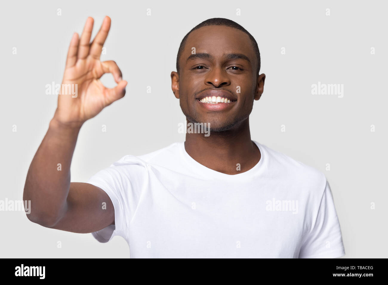 Felice maschio africana che mostra segno ok pongono su sfondo grigio Foto Stock