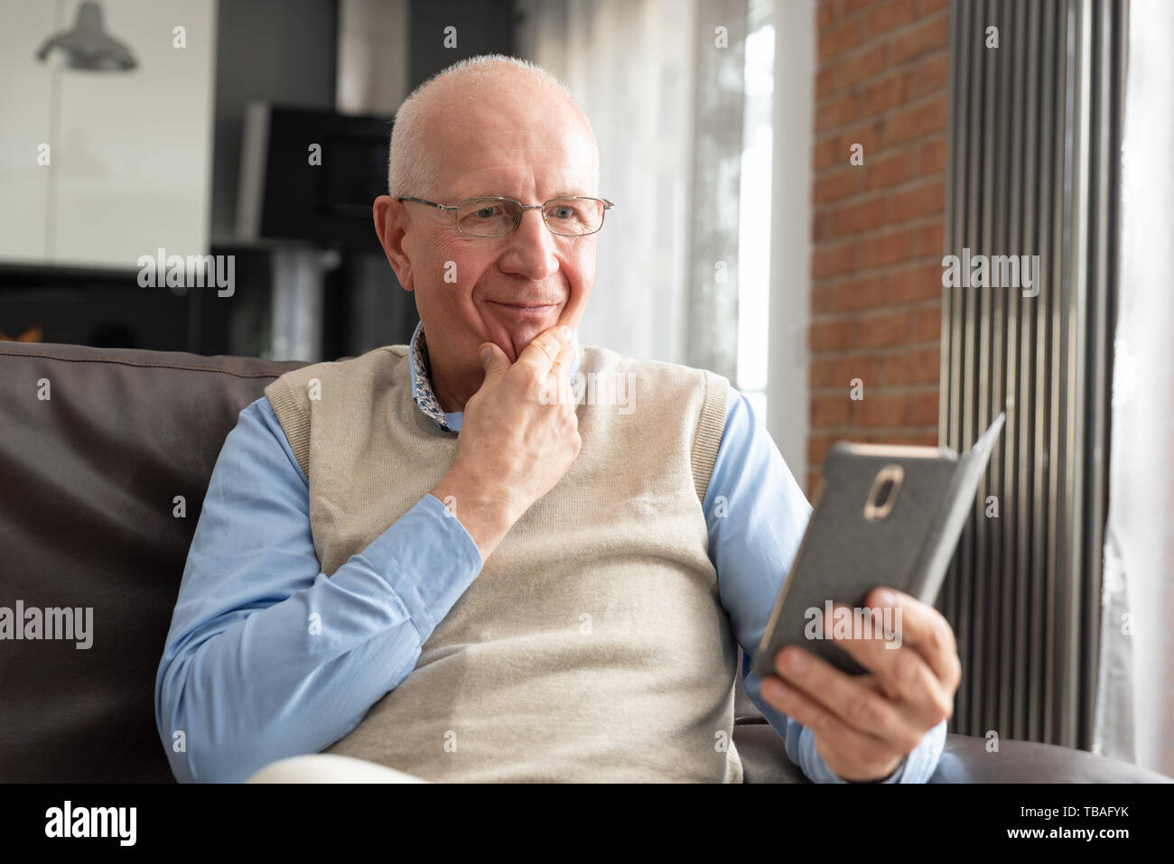 Senior uomo utilizzando uno smartphone e sorridente comodamente seduti sul divano di casa. Foto Stock