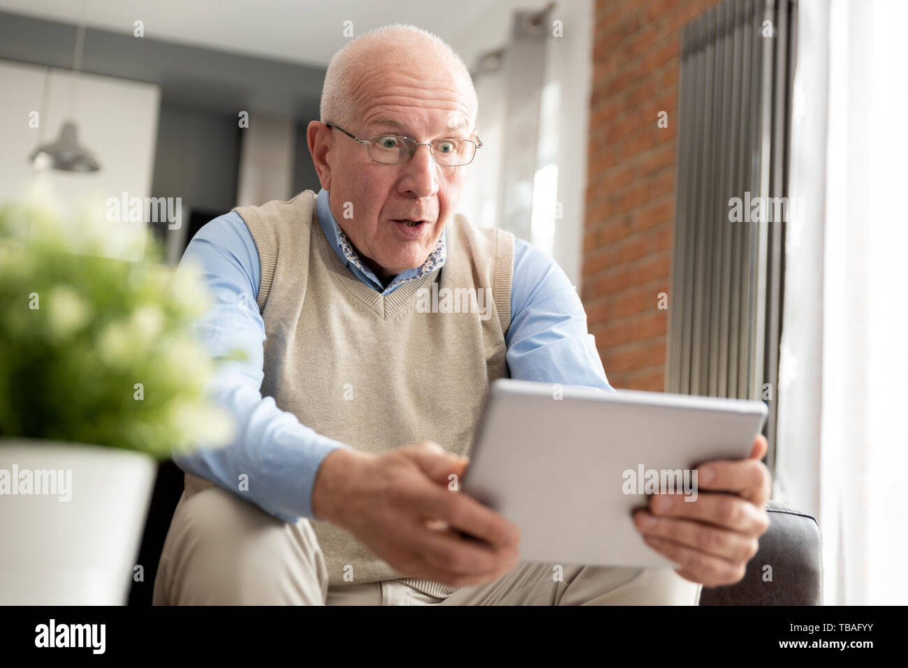Senior uomo sorpreso utilizzando una tavoletta digitale comodamente seduti sul divano di casa Foto Stock