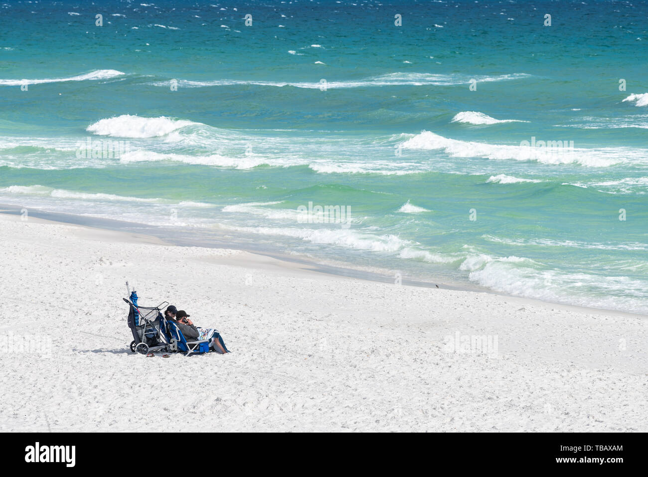 Destin, Stati Uniti d'America - 24 Aprile 2018: Miramar Beach al Golfo del Messico con coppia seduti su sedie a prendere il sole sulla sabbia di mare oceano onde si infrangono in estate Foto Stock