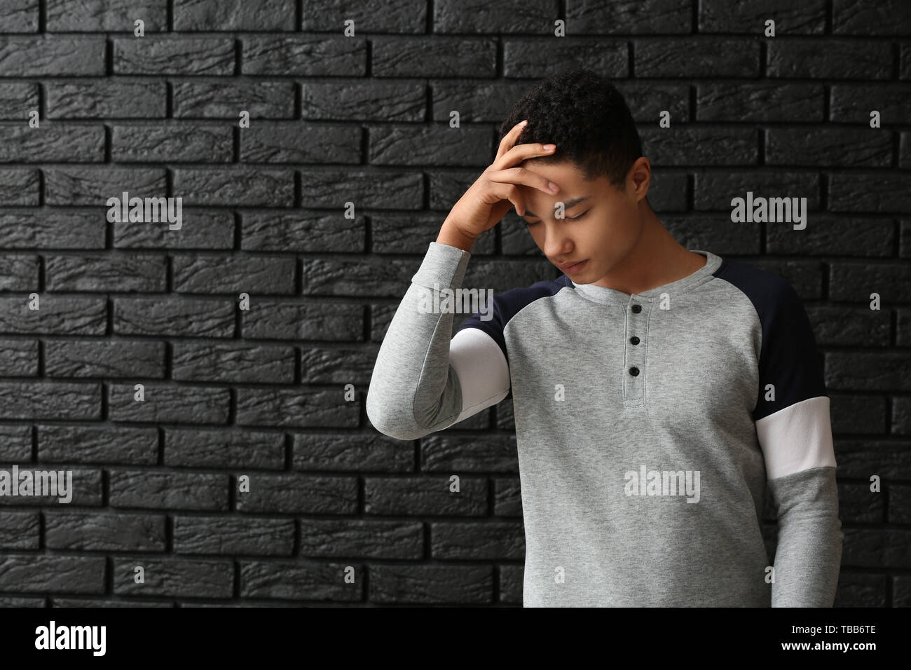 Triste ragazzo afro-americano dopo la mancata prova della scuola su sfondo scuro Foto Stock