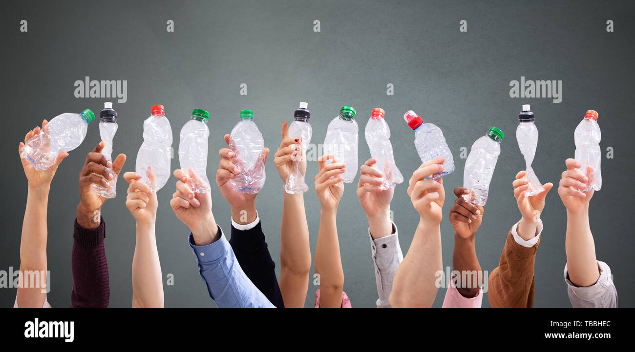 Gruppo di persone che la mano che tiene schiacciato le bottiglie di acqua contro uno sfondo scuro Foto Stock