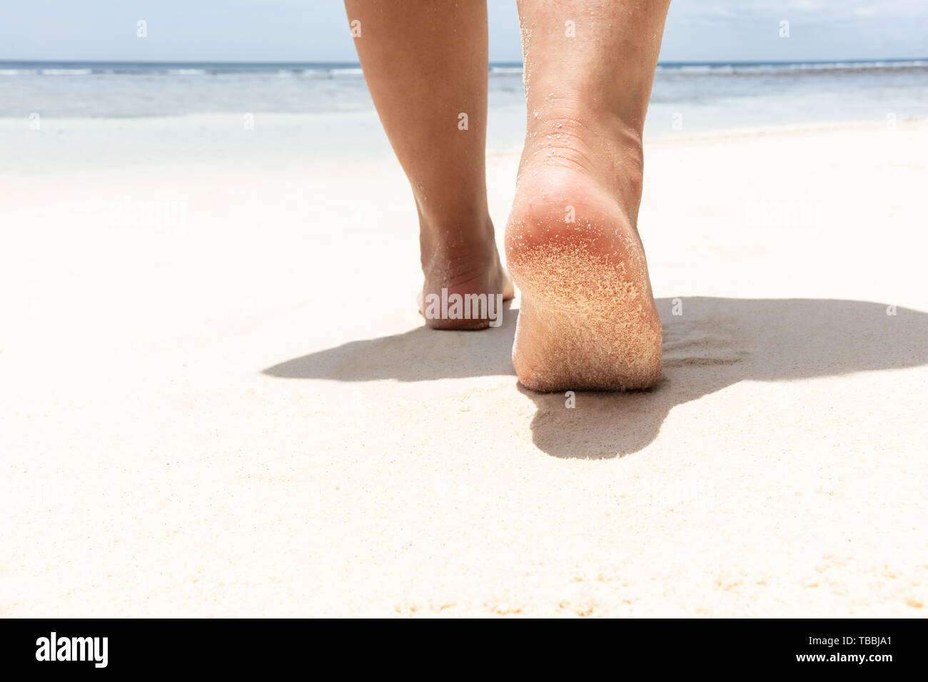 Sezione bassa della donna di piedi camminando sulla spiaggia sabbiosa verso il mare Foto Stock