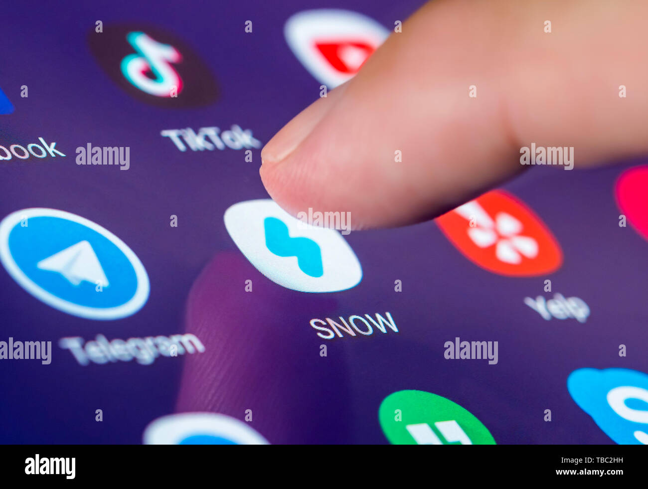 Dito che preme un'icona su uno smartphone o un tablet PC touchscreen per caricare la neve app Fotocamera, una immagine di messaggistica multimediale e social media applicazione. Foto Stock