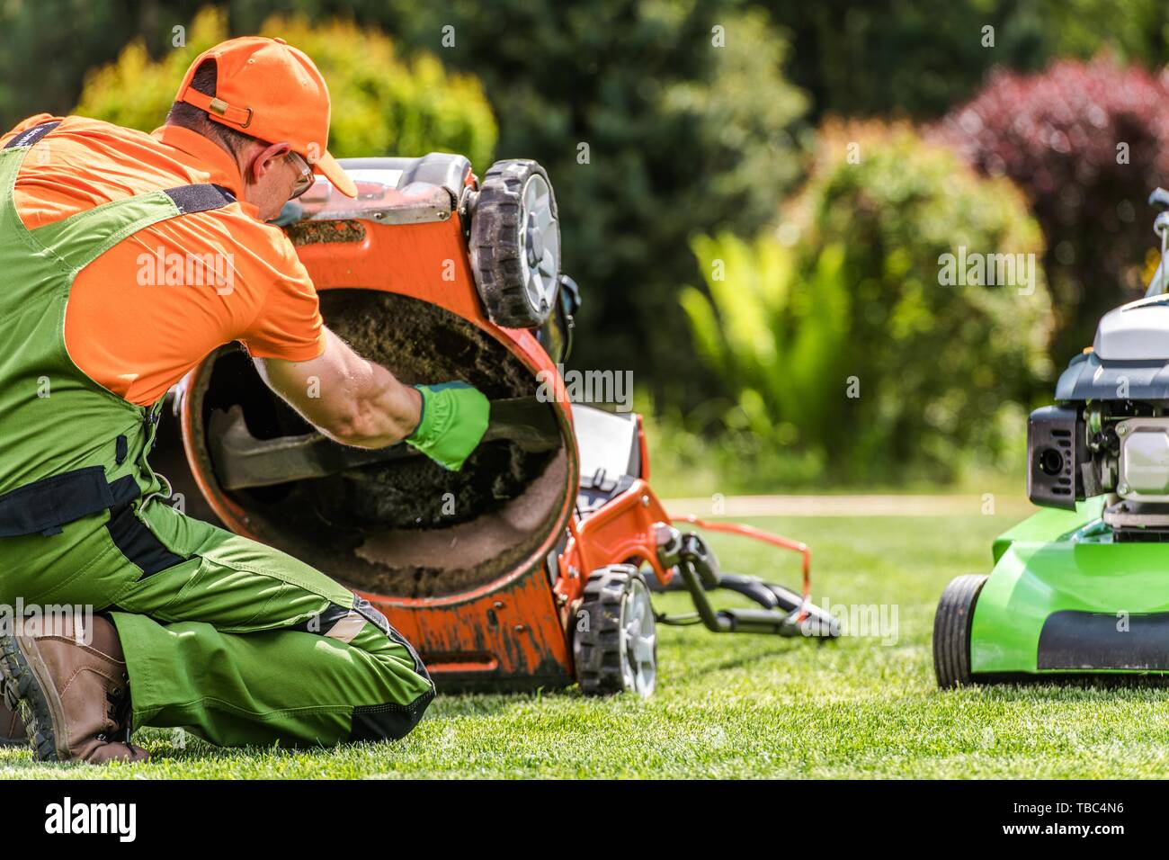 Falciatrice di erba problema. Giardiniere caucasico guardando sotto la macchina. Problema tecnico. Foto Stock