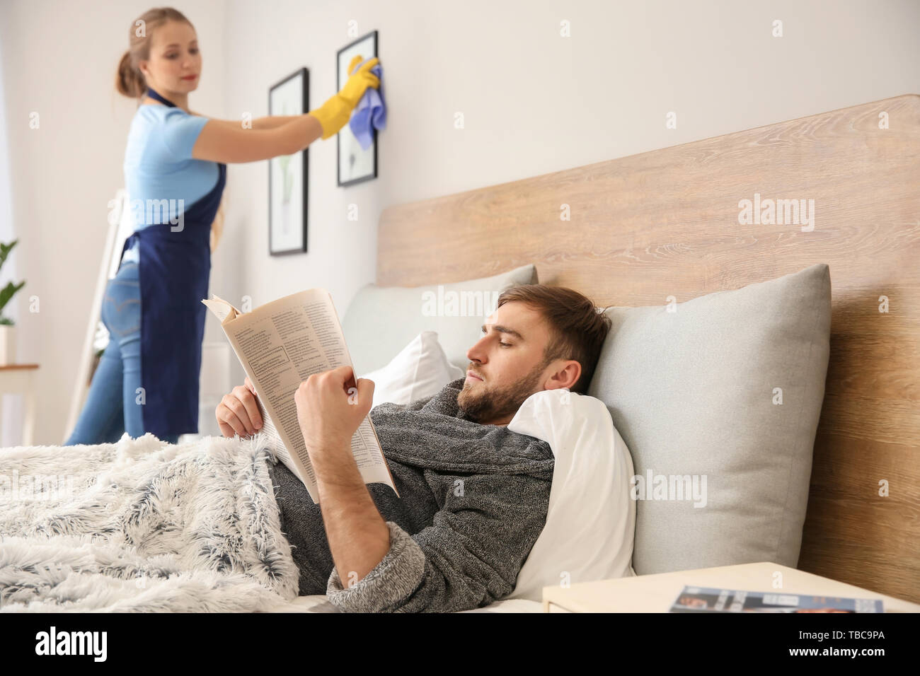 Lazy marito leggendo il giornale mentre sua moglie facendo faccende di casa Foto Stock