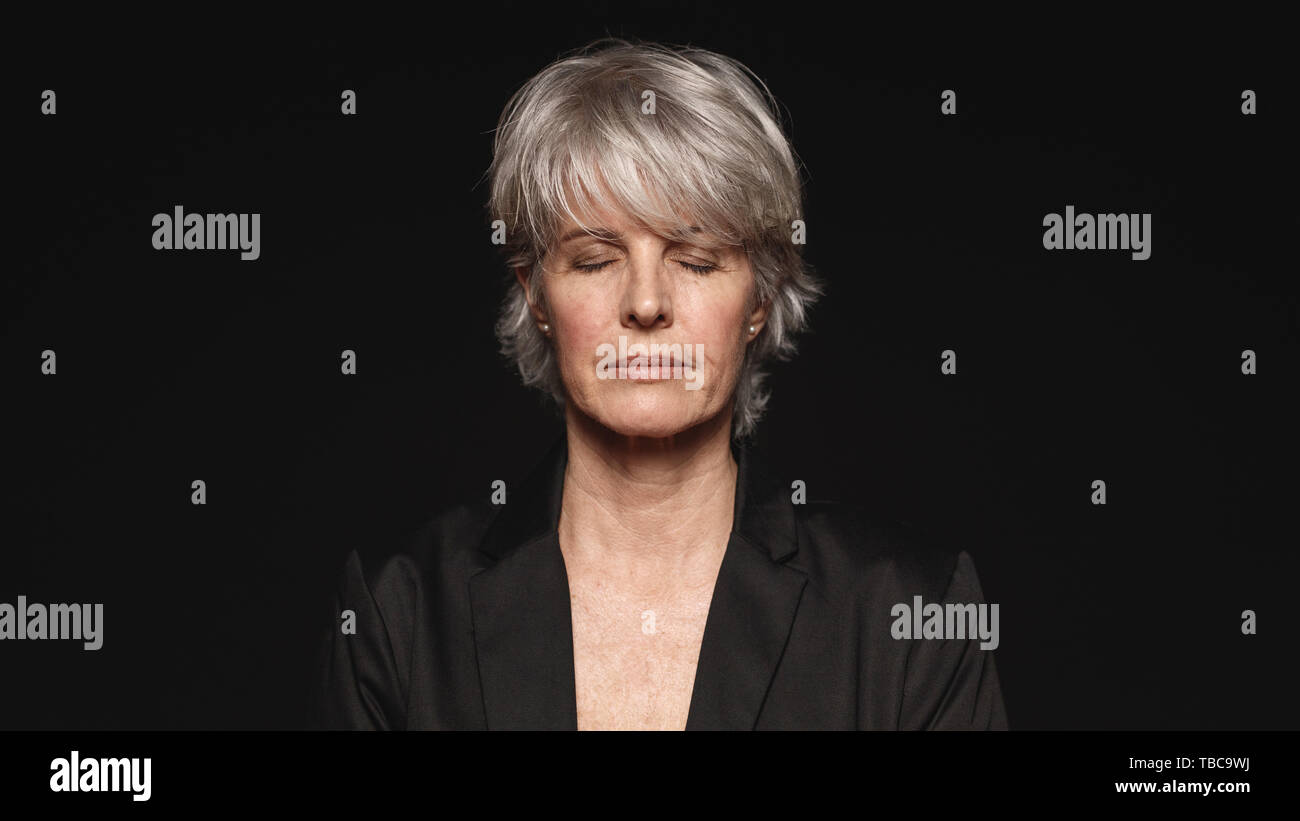 Close up di senior donna con gli occhi chiusi. Donna in abbigliamento formale isolati su sfondo nero. Foto Stock
