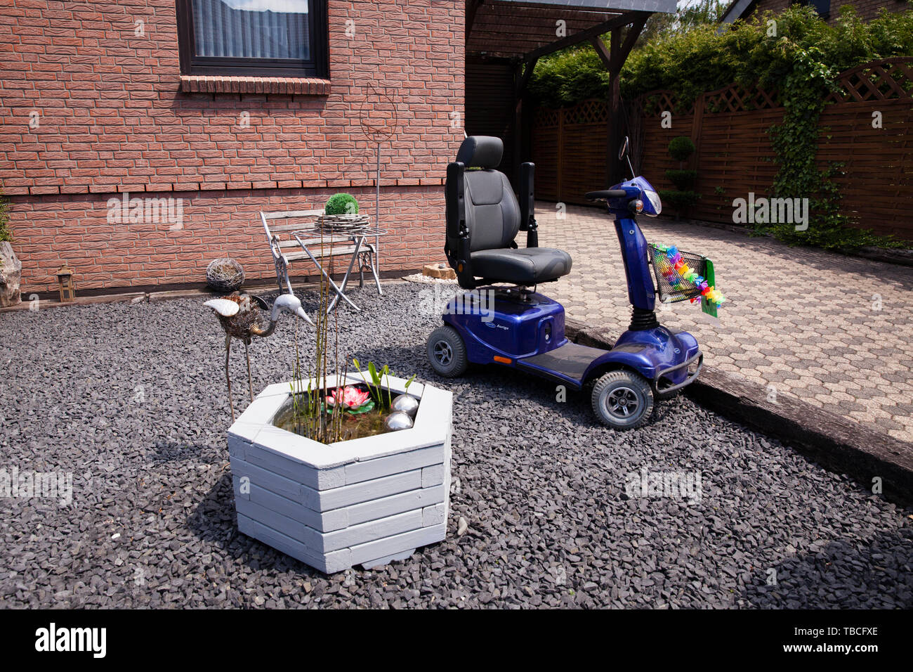 E-la sedia a rotelle in un cortile anteriore in Bergheim-Niederaussem, Germania. ein E-Rollstuhl steht in einem Vorgarten in Bergheim-Niederaussem, Steingarten, Deuts Foto Stock