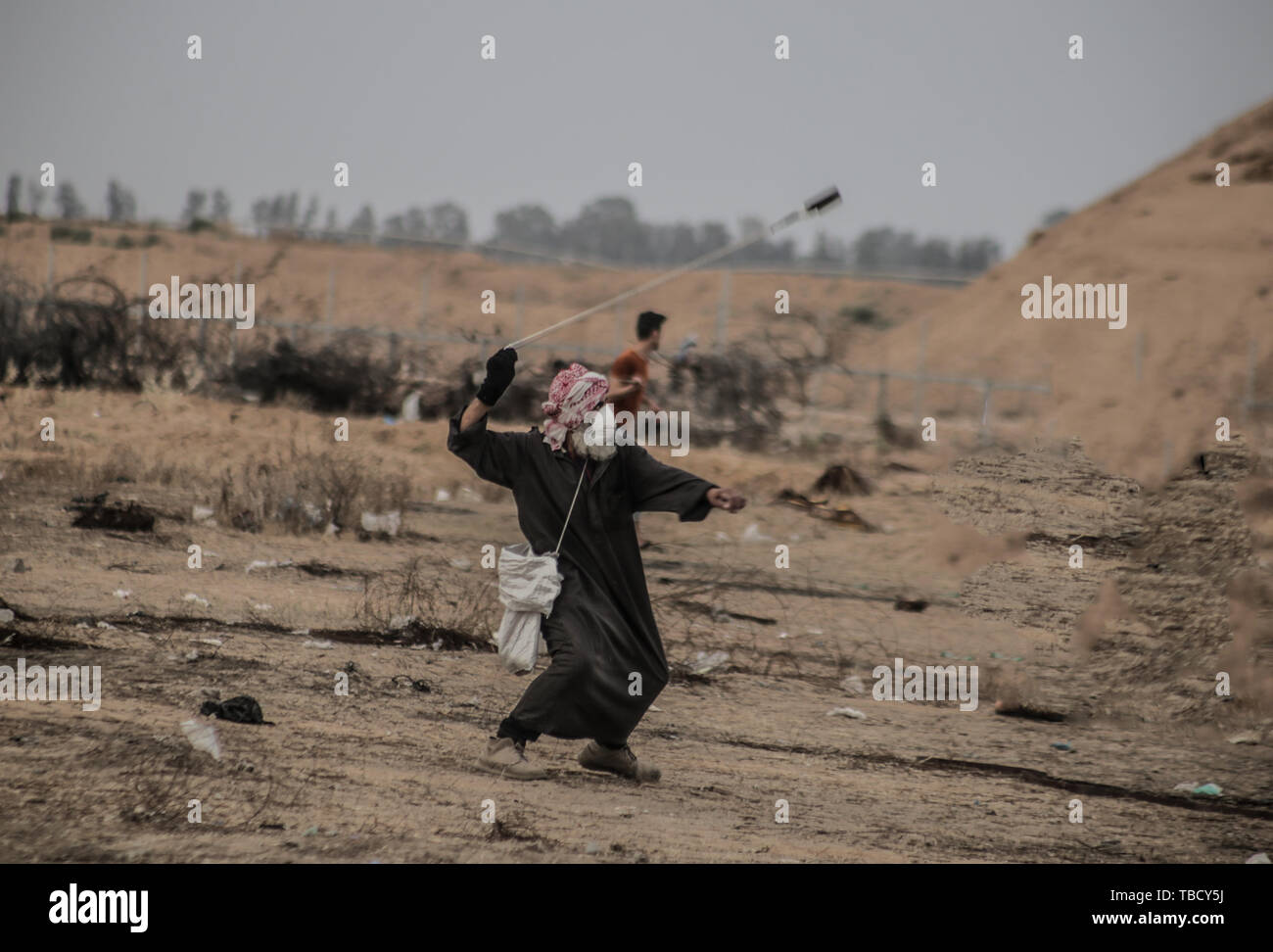 Un palestinese utilizza un slingshot a lanciare pietre verso le truppe israeliane durante gli scontri. I palestinesi si sono scontrati con le forze israeliane nel corso di una grande manifestazione sulla frontiera Gaza esigente per il diritto di tornare alle loro case durante la recinzione di confine tra Israele e la striscia di Gaza nel sud della striscia di Gaza. Foto Stock